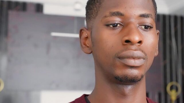 Black man closeup in studio, painted wall backdrop and soft light, contemplative expression with subtle gaze, cinematic moody portrait of young black painter and creative thinking