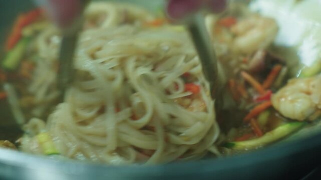 A cook stirs cooked noodles in a wok over a fire. Asian food. Cooking noodles. Stir-frying noodles with vegetables.