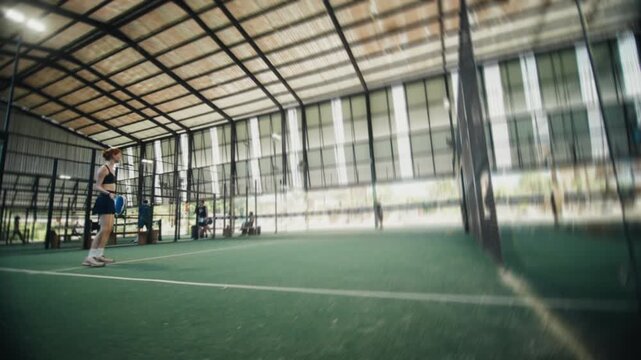 Female padel player serving ball in indoor court
