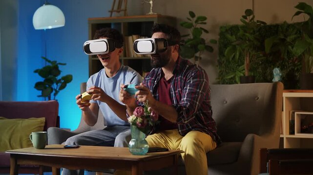 Father and his teen son in VR headsets playing video game with joysticks