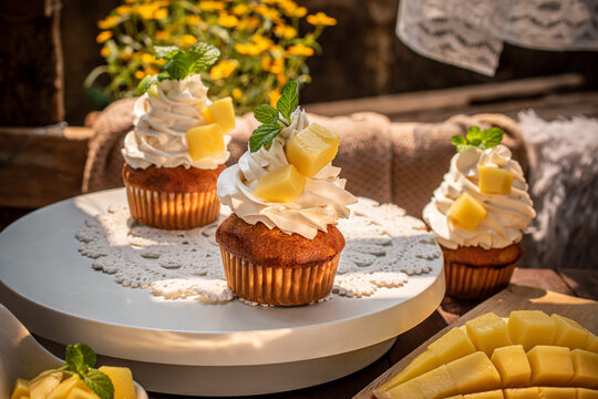 Delicious homemade mango cupcakes topped with smooth whipped cream, fresh mango cubes, and mint leaves on a white stand. Perfect for tropical summer dessert concepts and bakery cafe menus. 
