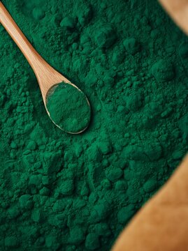 Vibrant green spirulina powder in a wooden spoon resting on a textured surface, showcasing the fine granules and rich color of the superfood ingredient