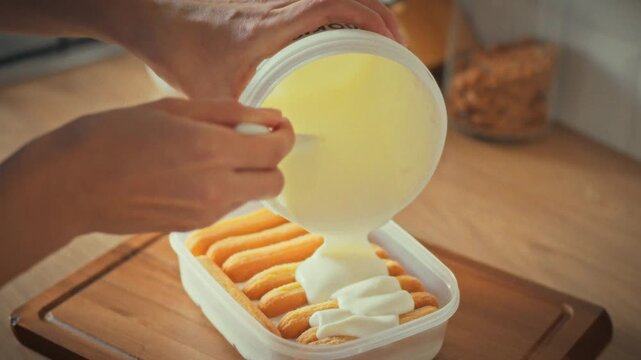 In cozy home kitchen, young housewife skillfully adds dollops of whipped cream to biscuits. Her baking process involves carefully crafting a sweet homemade dessert, perfecting her cake-making skills