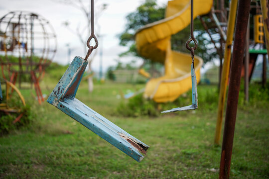 Broken plastic children's swing on the playground, old and unsafe swing. Old blue swing in an abandoned outdoor playground rustic environment