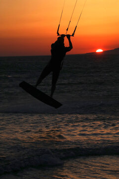 View of a kitesurfer silhouette jumping over the ocean waves during a vibrant sunset with an orange sky Tarifa, Andalusia, Spain.