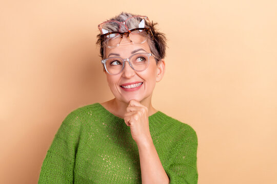 Happy mature lady model wearing green sweater with glasses thinking pose against beige background