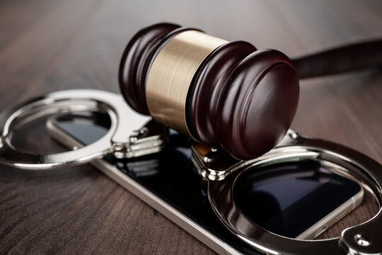 Wooden gavel and handcuffs on smartphone placed on round base. Concepts of court case in technology space and regulation.