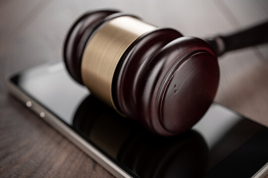 Wooden gavel on smartphone on the table. Concepts of app fraud, personal information leak and consumer protection.