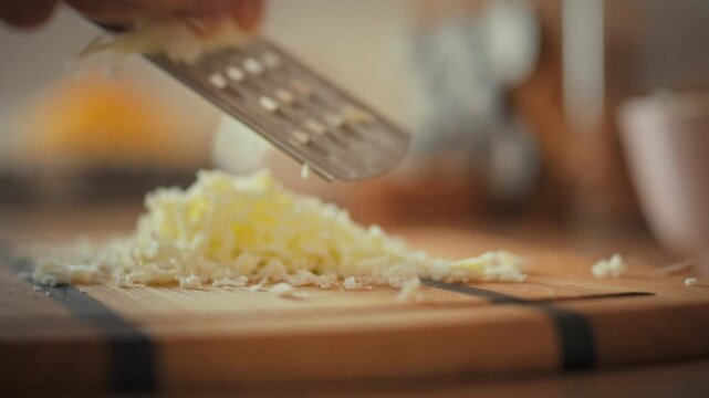 In a cozy home kitchen, a man's skilled hands expertly grate hard cheese using a grater. The simple process of preparing a meal highlights domestic culinary practices at home with everyday tools