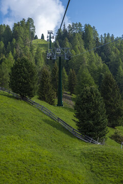 View of cable car gondolas ascending a lush green mountain slope with dense pine forests and a wooden fence in South Tyrol, Trentino-South Tyrol, Italy.