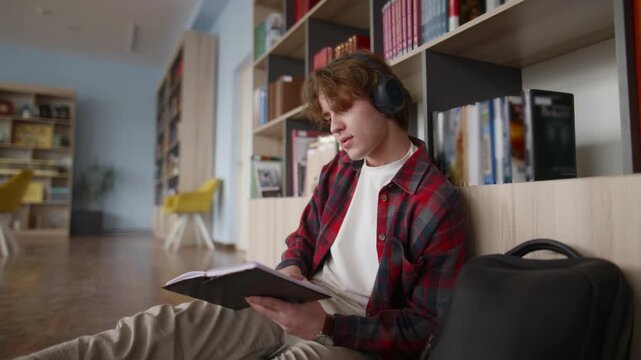 Focused student reading book and listening to music in library