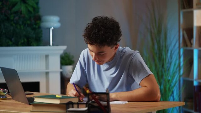Diligent teenage boy writing in notebook at home, preparing for exams