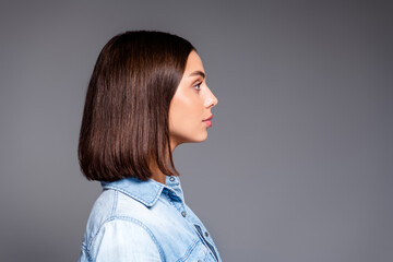 Young woman profile portrait in denim shirt with sleek bob hairstyle looking thoughtful on neutral gray background, studio side view beauty image conveying calm and confidence © deagreez