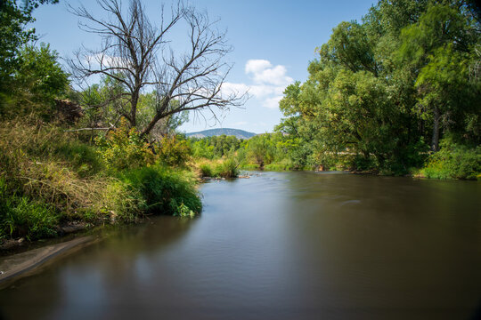 Smooth surface on the Big Thompson River of Colorado.  Blue sky and green trees line the river. Trees in Colorado springtime with lush green foliage.  Glassy surface of long exposure.