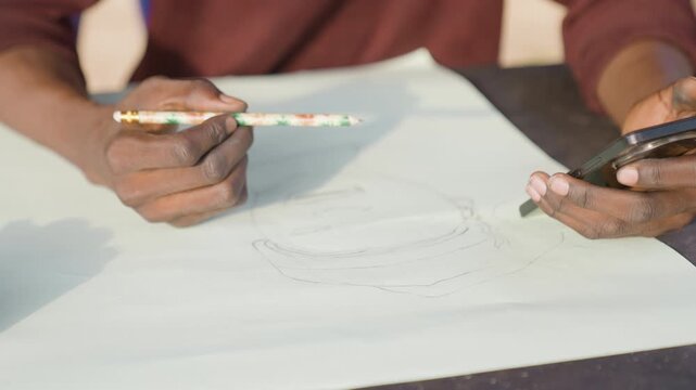 Black artist sketching portrait with phone, hands alternate between smartphone and pencil using photo reference to refine dotted outline and shading, outdoor table setting with warm sunlight,
