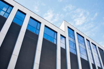 Fototapeta premium Modern glass office building facade on a sunny day under bright blue sky with white clouds. Big city life, contemporary architecture, offline business style background.