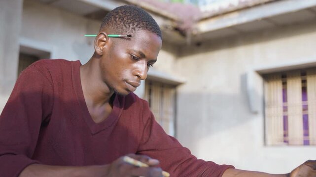 Black painting sketch session, calm illustrator concentrating on linework with pencil and pen, maroon sweater, courtyard architecture in background, steady patient posture and thoughtful expression