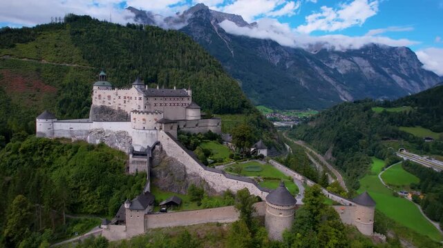 Cinematic Aerial 4K View of Hohenwerfen Castle on Green high mountain. Majestic Medieval Fortress Surrounded by Misty Austrian Alps and Clouds. Historic Landmark in Salzburg Region Austria. slow drone