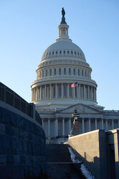Last beams of golden sunlight on the United States Capitol Building in Washington, DC, with the American flag waving, blue sky backrgound