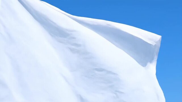Close-up view of a white flag waving against a bright blue sky on a sunny day