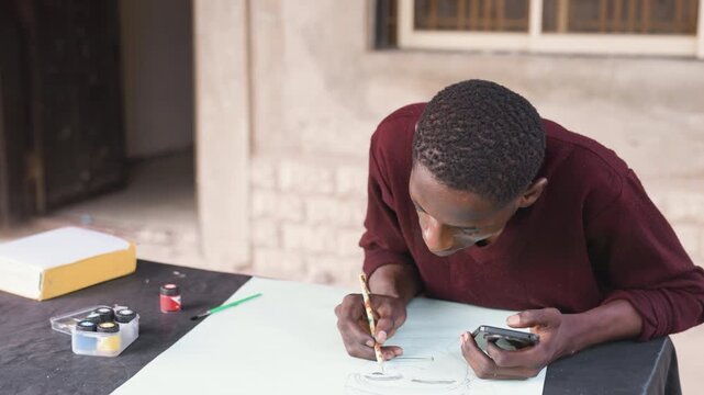 Outdoor black man painting on table, pale sheet of paper and jars of paint nearby, maroon sweater, porch backdrop and window, slow finishing strokes and calm reflective mood, steady hand composing