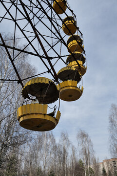 View of the abandoned yellow Ferris wheel in the amusement park of the Chernobyl exclusion zone with bare trees in Pryp'yat', Kyiv Oblast, Ukraine.
