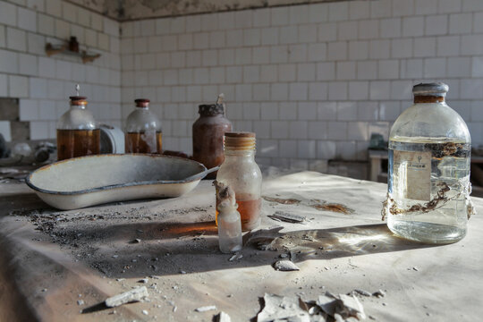 View of abandoned medical glass bottles and a metal kidney dish on a dusty table in a derelict hospital room in Pripyat, Kyiv Oblast, Ukraine.