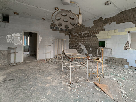 View of an abandoned operating room with a surgical lamp, metal table, and peeling tiles on the walls in Pryp'yat', Kyiv Oblast, Ukraine.