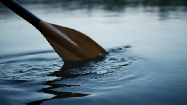 Canoe paddle dipping into blue water lake. Outdoors recreation, paddling.