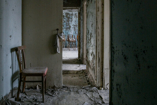 View of an abandoned room with a wooden chair, peeling paint on walls, and debris on the floor in Pryp'yat', Kyiv Oblast, Ukraine.