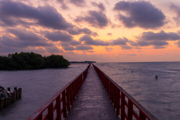 Obraz premium A view of the red bridge crossing the sea at sunrise,A stunning long-exposure photograph featuring a vibrant red wooden bridge stretching toward the horizon over the calm sea. The scene is captured.