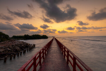 Obraz premium A view of the red bridge crossing the sea at sunrise,A stunning long-exposure photograph featuring a vibrant red wooden bridge stretching toward the horizon over the calm sea. The scene is captured.
