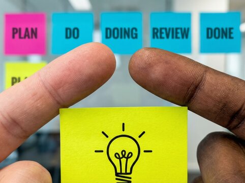 Close-up view of diverse hands uniting over a bright idea, symbolizing collaborative innovation and the systematic journey of a project from planning to successful completion