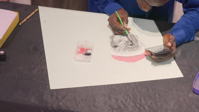 Black artist demonstrating portrait wash technique, darkskinned male guiding brush across white sheet, controlled black ink and gray washes layered over pink shape, phone reference and palette