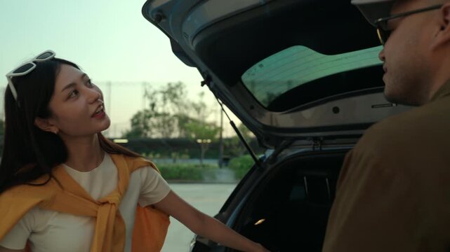  Happy young couple lifting luggage into car near airport. Travel preparation in road trip. Summer vacation and modern travel lifestyle with safe driving concept.
