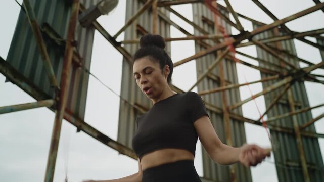 Young Black woman in activewear exercising with jump rope on rooftop, training