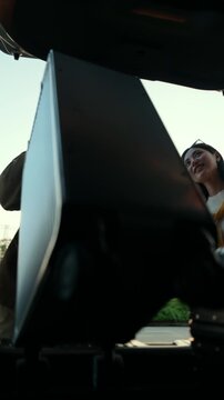  Happy young couple lifting luggage into car near airport. Travel preparation in road trip. Summer vacation and modern travel lifestyle with safe driving concept.
