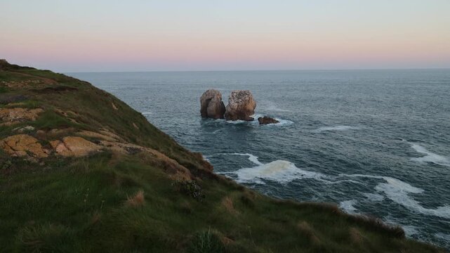 View of the Urros de Liencres sea stacks and rugged coastline under a soft twilight sky in Liencres, Cantabria, Spain.