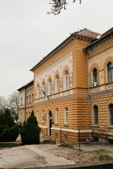 Fototapeta premium Historic yellow building with decorative facade located in Zrenjanin, Serbia under cloudy sky. European architecture and urban city concept.