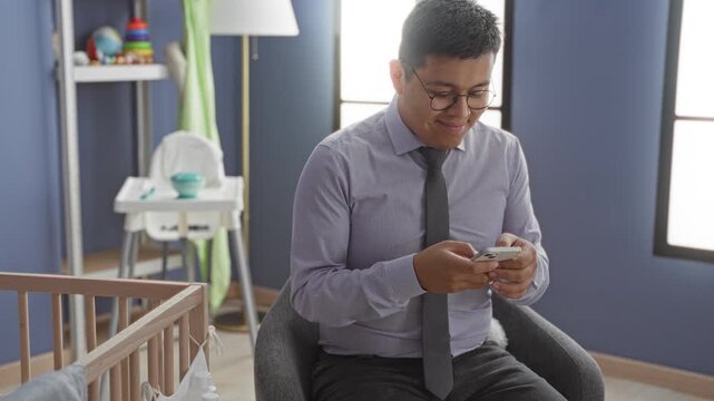 Man in dress shirt and tie holding smartphone, hands tapping screen beside wooden baby crib and highchair in building; quiet parental tenderness.