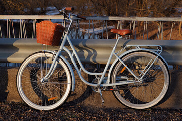 Obraz premium A bicycle with a brown basket is parked next to a guardrail during a sunny day. The river and trees are visible in the background