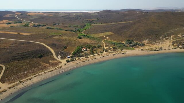 High-angle aerial view of the Neftina Beach on Limnos Island, Greece, showing crystal clear turquoise waters meeting a sandy shoreline backed by rugged, arid Mediterranean hills.