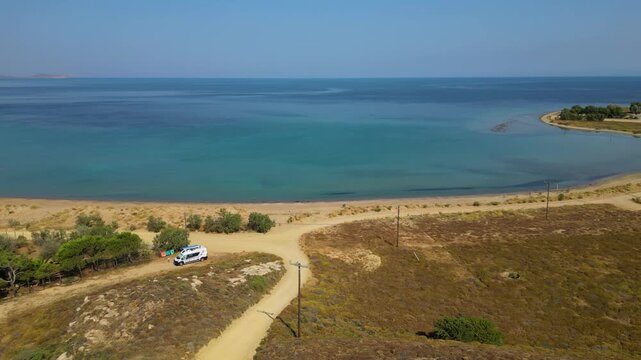 High-angle aerial view of the Neftina Beach on Limnos Island, Greece, showing crystal clear turquoise waters meeting a sandy shoreline backed by rugged, arid Mediterranean hills.