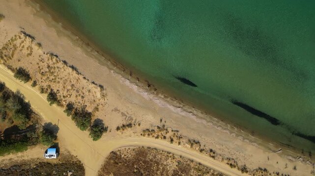High-angle aerial view of the Neftina Beach on Limnos Island, Greece, showing crystal clear turquoise waters meeting a sandy shoreline backed by rugged, arid Mediterranean hills.