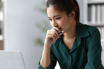 Stressed Asian businesswoman looking worriedly at laptop screen while working in office.