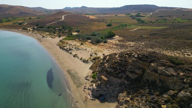 High-angle aerial view of the Neftina Beach on Limnos Island, Greece, showing crystal clear turquoise waters meeting a sandy shoreline backed by rugged, arid Mediterranean hills.