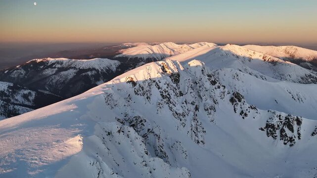 Aerial view of snow-capped Dumbier mountains under a soft, golden sky, with contrasting shadows accentuating the rugged peaks, Nizke Tatry, Zilina Region, Slovakia.