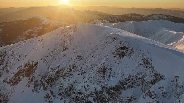 Aerial view of Dumbier mountain peak covered with snow, as the sun sets, casting long shadows across the rugged landscape, Nizke Tatry, Zilina Region, Slovakia.