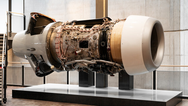 Jet engine undergoing maintenance in repair facility. Side-view of a large turbofan aircraft engine with removed cowling mounted on a service stand in a modern maintenance hangar.