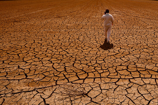Man walking across cracked dry ground in a dried landscape during drought. Concept of climate change, desertification and environmental crisis.